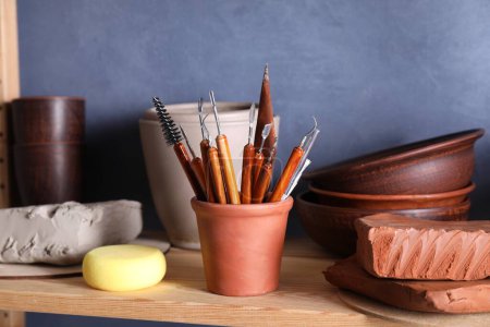Ensemble de différents outils d'artisanat et plats en argile sur support en bois dans l'atelier, gros plan