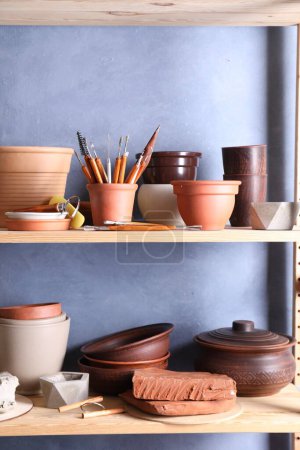 Ensemble de différents outils d'artisanat et plats en argile sur support en bois dans l'atelier