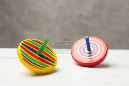 Two bright spinning tops on white table, closeup
