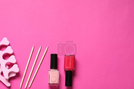 Foto de Esmaltes de uñas, palos naranjas y separadores de dedos sobre fondo rosa, posición plana. Espacio para texto - Imagen libre de derechos