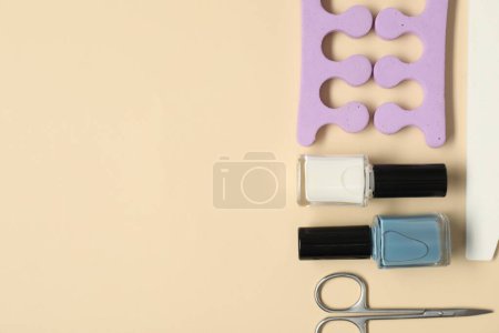 Nail polishes, scissors, toe separators and file on beige background, flat lay. Space for text