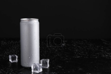 Energy drink in wet can and ice cubes on black textured table, space for text