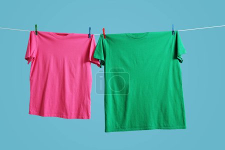 Bunte T-Shirts trocknen auf Waschschnur vor hellblauem Hintergrund