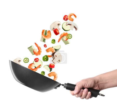 Hombre lanzando ingredientes en wok sobre fondo blanco, primer plano