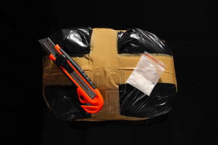 Schmuggel, Drogenhandel. Pakete mit Betäubungsmitteln und Gebrauchsmesser auf schwarzer Oberfläche, Ansicht von oben
