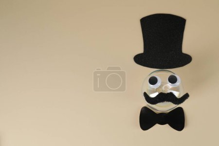 Téléchargez les photos : Visage d'homme en fausse moustache, boule, chapeau, noeud papillon et yeux sur fond beige, vue de dessus. Espace pour le texte - en image libre de droit