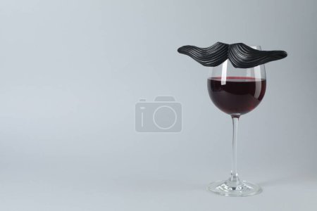 Téléchargez les photos : Verre de vin rouge avec drôle de fausse moustache sur fond gris, espace pour le texte - en image libre de droit