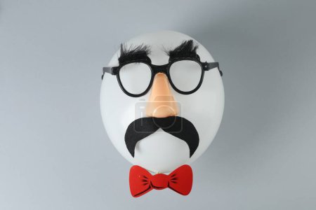 Téléchargez les photos : Visage d'homme en ballon, masque drôle avec fausse moustache, nez et lunettes sur fond gris, vue de dessus - en image libre de droit