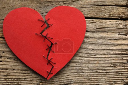 Coeur brisé. Coeur en papier rouge déchiré cousu avec du fil sur une table en bois, vue de dessus. Espace pour le texte
