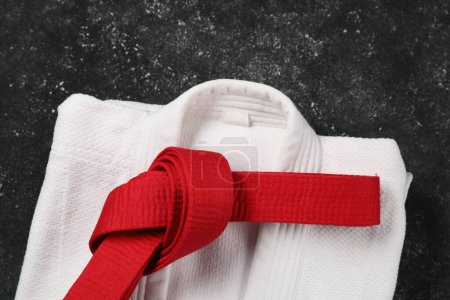 Red karate belt and white kimono on gray textured background, top view