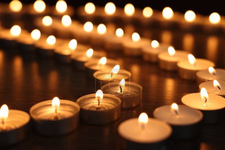 Brennende Kerzen auf Holztisch in der Dunkelheit, Nahaufnahme