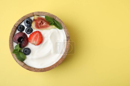 Cuenco con yogur, bayas, frutas y menta sobre fondo amarillo, vista superior. Espacio para texto