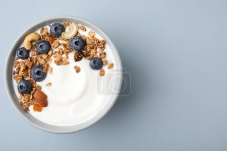 Cuenco con yogur, arándanos y granola sobre fondo gris claro, vista superior. Espacio para texto