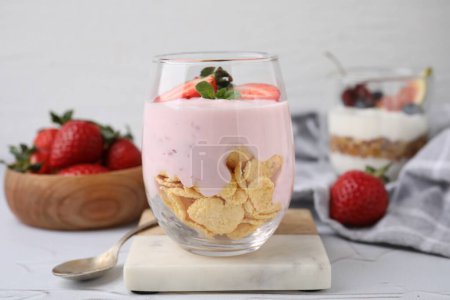 Vidrio con yogur, fresas y hojuelas de maíz sobre mesa blanca texturizada