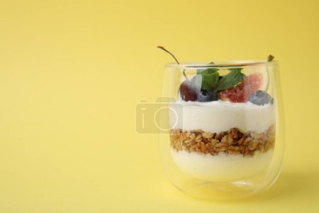 Vidrio con yogur, bayas y granola sobre fondo amarillo. Espacio para texto