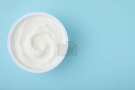 Delicioso yogur natural en taza de plástico sobre fondo azul claro, vista superior. Espacio para texto