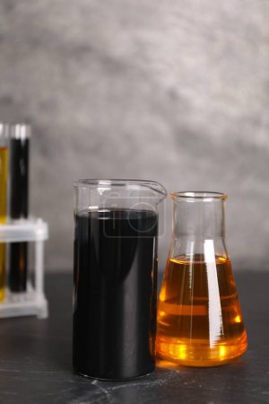 Beaker, flask and test tubes with different types of oil on grey textured table