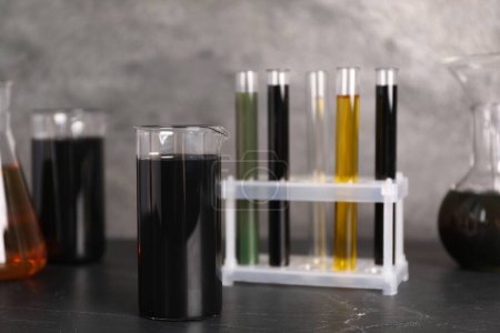 Photo for Beakers, flasks and test tubes with different types of oil on grey textured table, closeup - Royalty Free Image