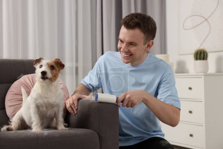 Hombre sonriente quitando el pelo de la mascota del sillón en casa