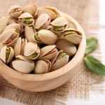 Tasty pistachios in bowl on white wooden table, closeup