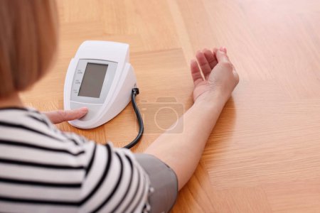 Foto de Mujer midiendo su presión arterial con tonómetro en mesa de madera en el interior, primer plano - Imagen libre de derechos