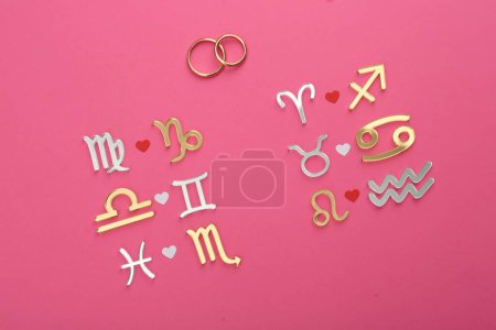 Foto de Compatibilidad con el zodiaco. Signos y anillos de boda sobre fondo rosa, planas - Imagen libre de derechos