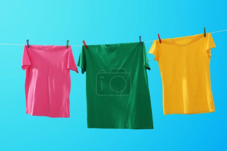 Bunte T-Shirts trocknen auf Waschschnur vor hellblauem Hintergrund