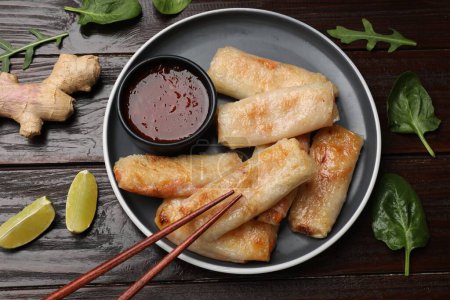 Tasty fried spring rolls, lime, sauce and other products on wooden table, flat lay