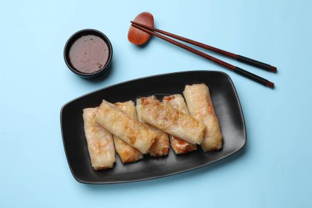 Fried spring rolls and sauce served on light blue table, top view
