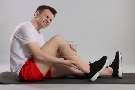 Mann leidet unter Beinschmerzen auf Matte vor grauem Hintergrund