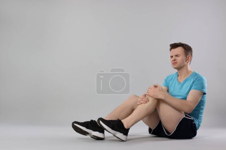 Man suffering from leg pain on grey background. Space for text
