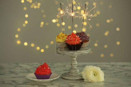 Verschiedene bunte Cupcakes mit Wunderkerzen auf weißem Marmortisch gegen verschwommenes Licht
