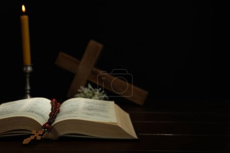 Crosses, rosary beads, Bible and church candle on wooden table, space for text