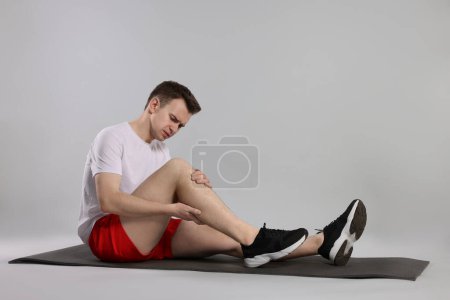 Photo for Man suffering from leg pain on mat against grey background - Royalty Free Image