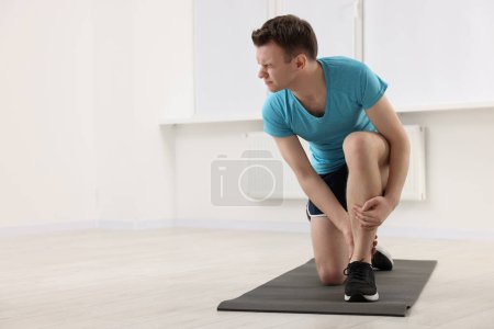 Man suffering from leg pain on mat indoors. Space for text