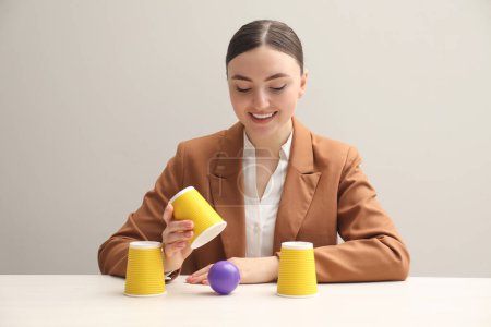 Juego de Shell. Mujer feliz mostrando la pelota debajo de la taza en la mesa blanca