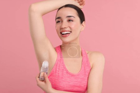 Hermosa mujer aplicando desodorante sobre fondo rosa