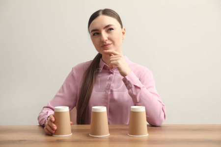 Thoughtful woman playing shell game at wooden table