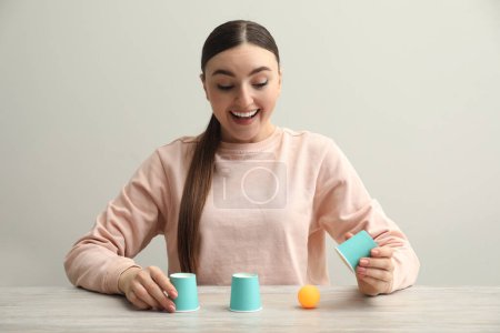 Shell game. Happy woman showing ball under cup at wooden table
