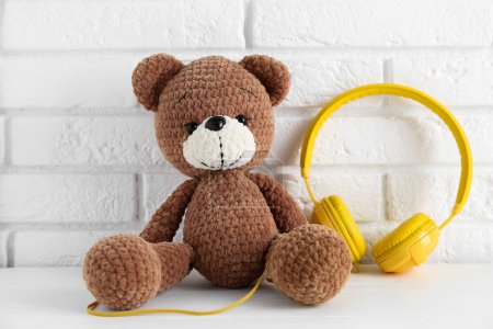 Baby songs. Toy bear and yellow headphones on white wooden table