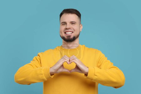 Mann zeigt Herz-Geste mit Händen auf hellblauem Hintergrund