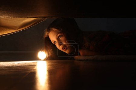 Photo for Little girl with flashlight looking for monster under bed at night - Royalty Free Image