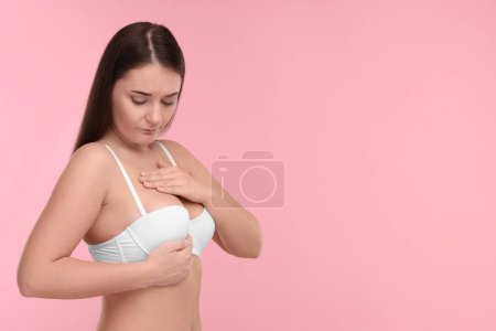 Mamología. Mujer en sujetador haciendo auto-examen de pecho sobre fondo rosa, espacio para el texto