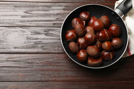 Roasted edible sweet chestnuts in frying pan on wooden table, top view. Space for text
