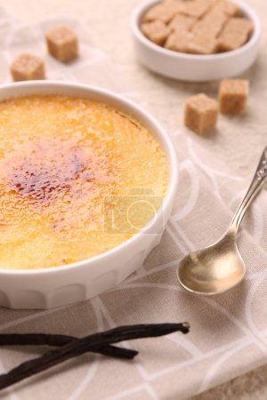 Delicious creme brulee in bowl, vanilla pods and spoon on table, closeup