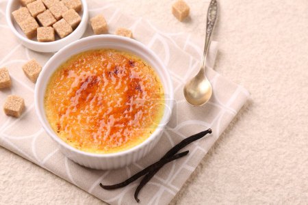 Photo for Delicious creme brulee in bowl, vanilla pods, sugar cubes and spoon on light textured table, closeup - Royalty Free Image
