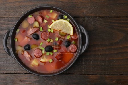 Fleischsoljanka-Suppe mit dünnen, trockenen geräucherten Würstchen in Schüssel auf Holztisch, Draufsicht. Raum für Text