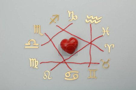 Foto de Compatibilidad con el zodiaco. Signos, corazón rojo e hilos sobre fondo gris, posición plana - Imagen libre de derechos