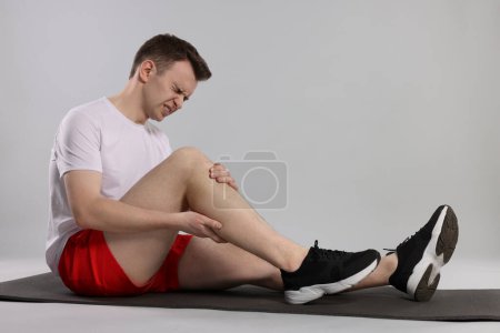 Mann leidet unter Beinschmerzen auf Matte vor grauem Hintergrund