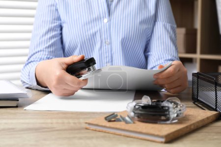 Woman with papers using stapler at wooden table indoors, closeup